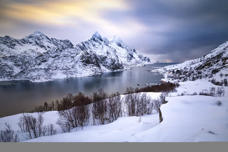 Paysage d'hiver spectaculaire avec un lac aux eaux sombres entouré de montagnes escarpées couvertes de neige, typique des décors naturels à découvrir en Ariège.