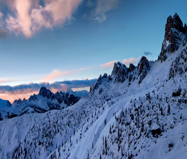 Panorama majestueux sur les sommets rocheux des Dolomites sous la neige au coucher du soleil, évoquant la beauté sauvage de la haute montagne en hiver.