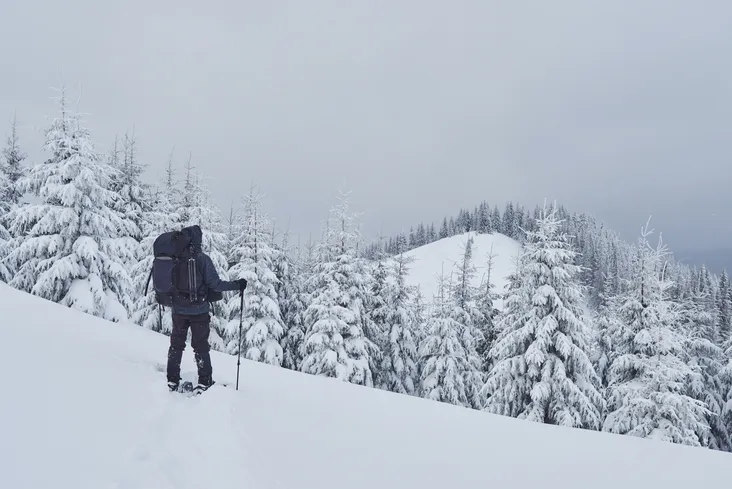 Un randonneur équipé d'un grand sac à dos et de bâtons contemple un sommet enneigé dans les Pyrénées, illustrant les activités de plein air accessibles depuis un camping ouvert à l'année en Ariège